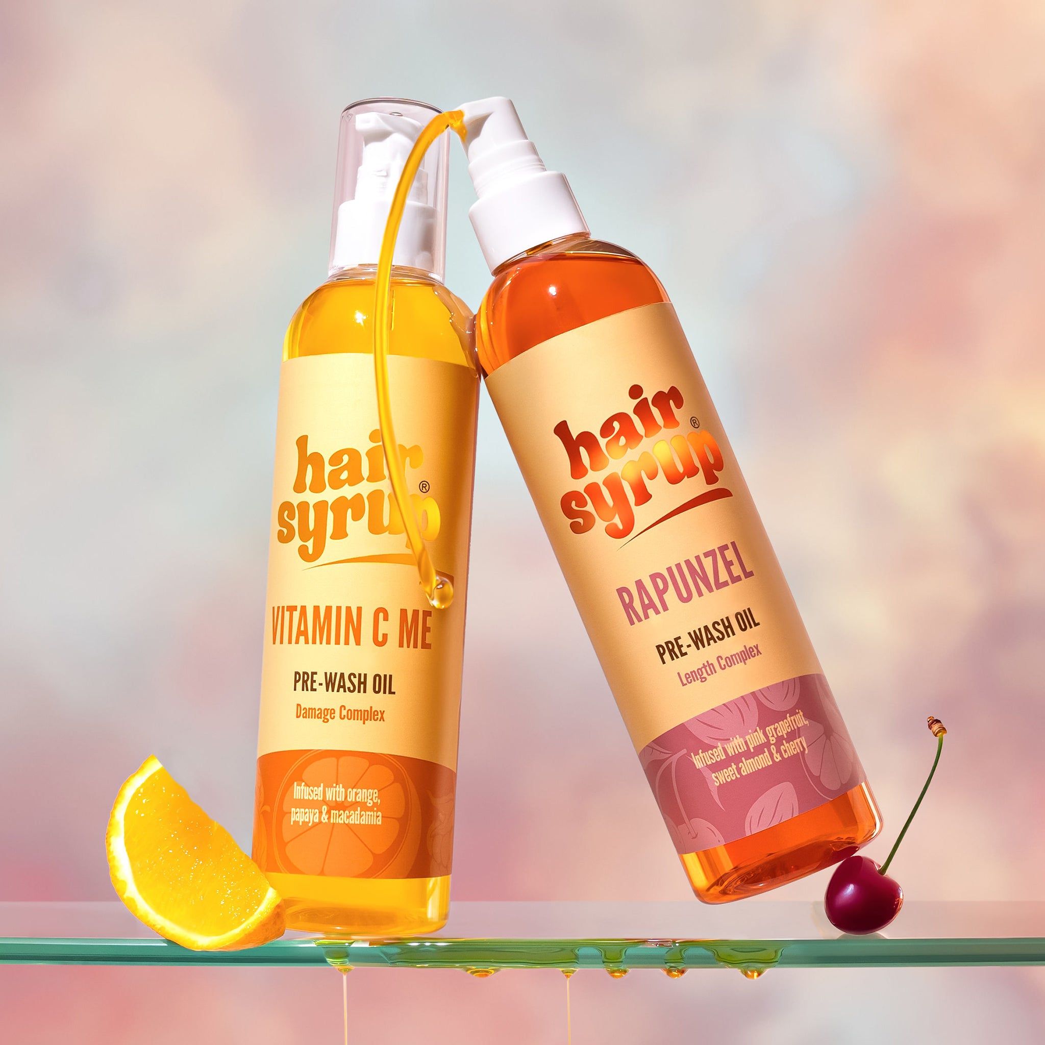 Twee flessen "Hair Syrup" producten. "Vitamin C Me" en "Rapunzel". Pre-Wash Oil. Op glazen plaat.