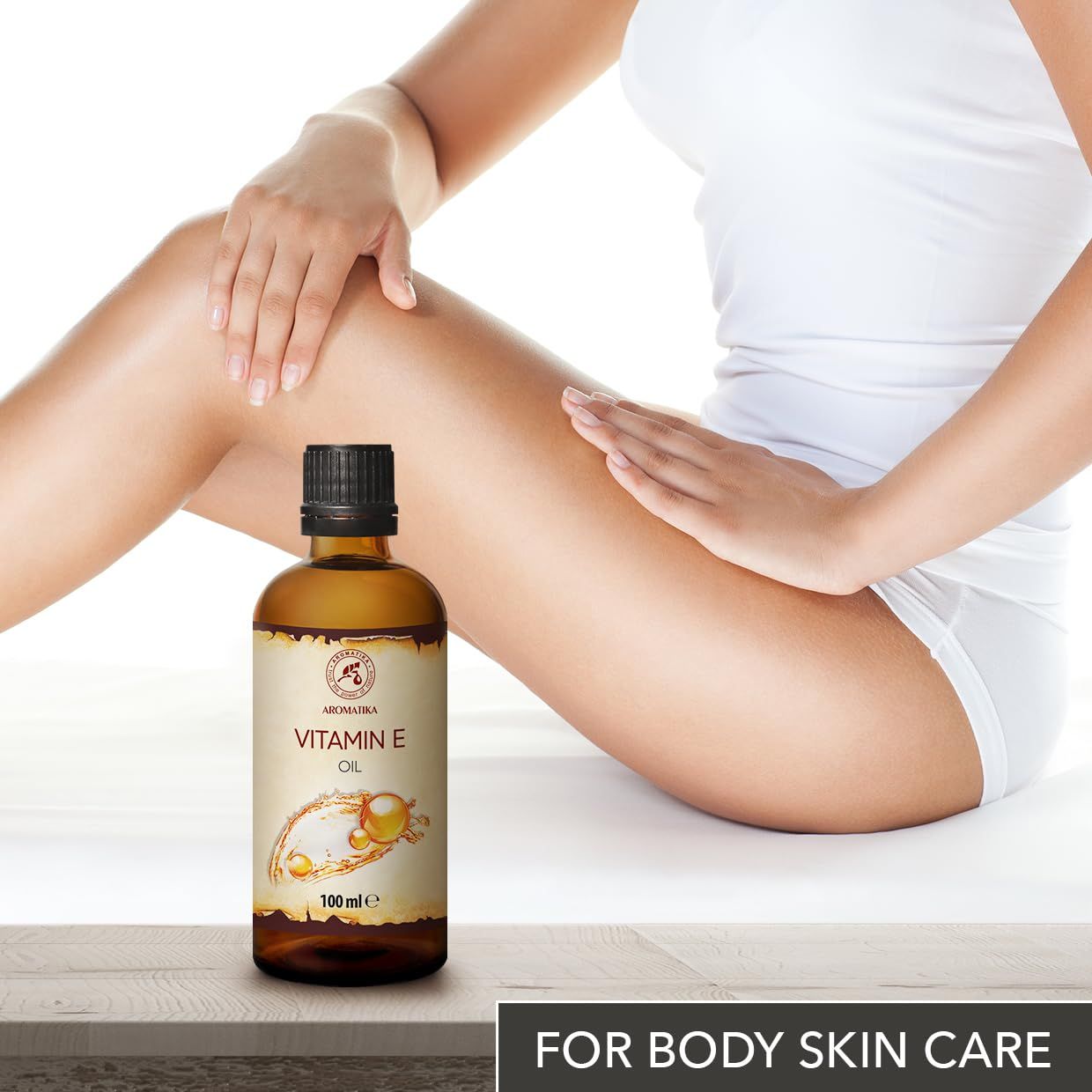 Vrouw met ingeoliede benen, naast AROMATIKA Vitamine E Olie fles. Tekst "For Body Skin Care".