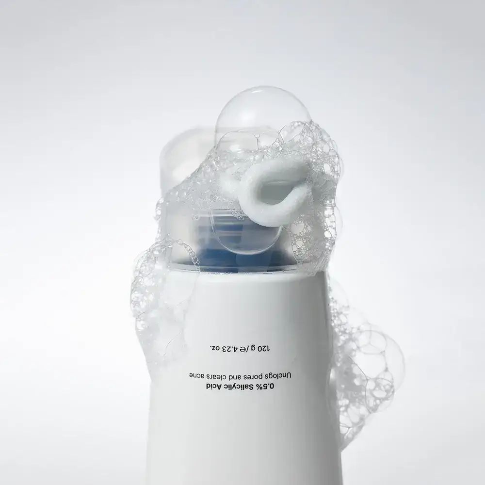 Witte tube met schuim. Opschrift: 0,5% Salicylzuur. 120 g / 4,23 oz. Schuim bedekt de bovenkant.