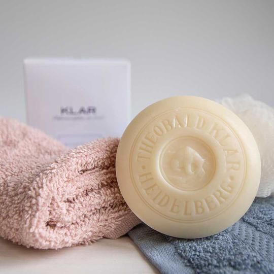 Ronde zeep, handdoek, badspons en verpakking met Klar-logo en 'Badeseife Damen'.