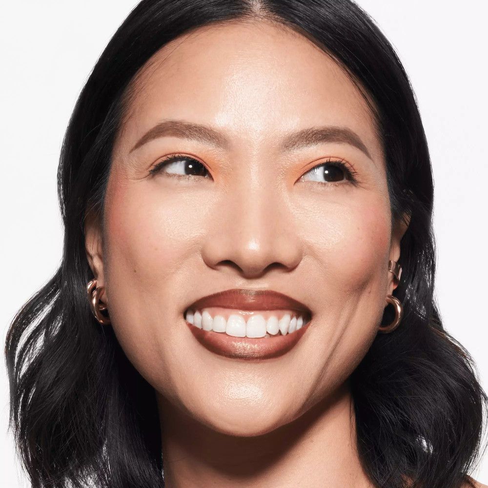 Portret van een lachende vrouw met bruine lippenstift. Ze draagt gouden oorbellen.