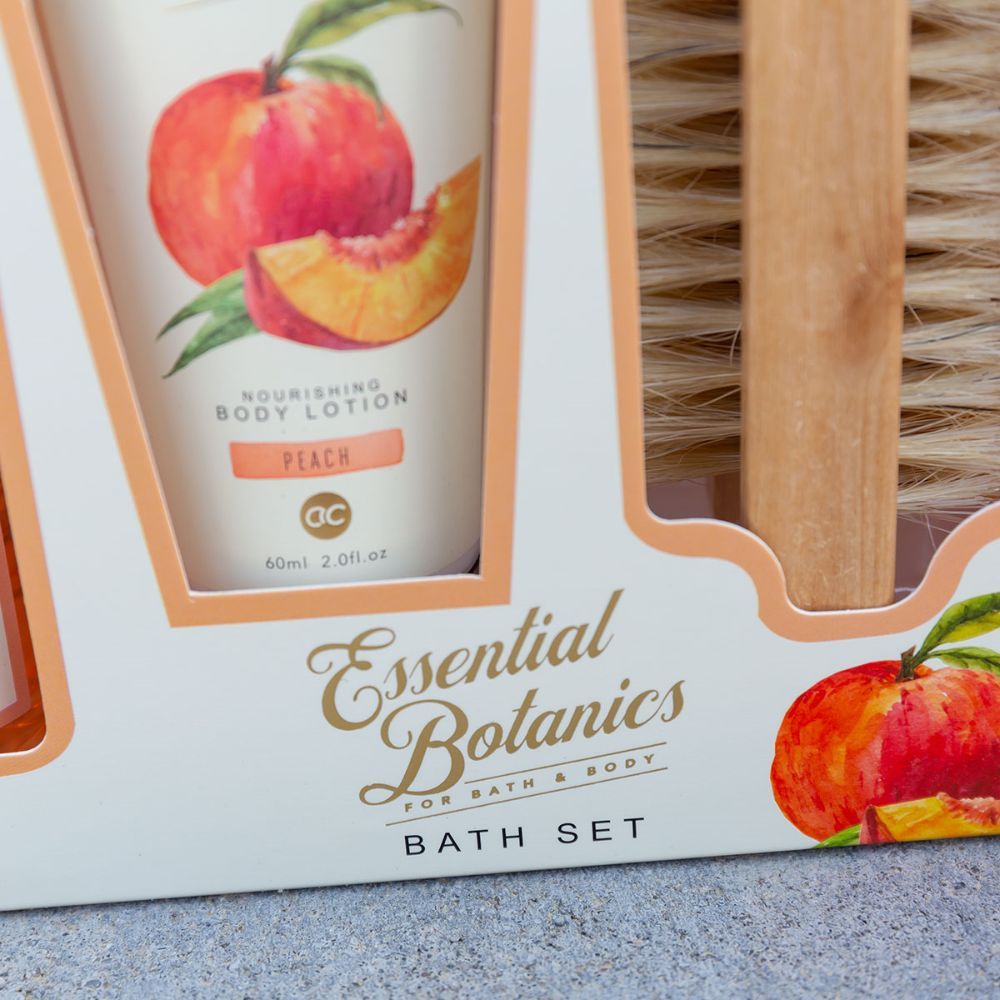 Gros plan sur le coffret cadeau. Affiche l'inscription "Essential Botanics" et "Bath Set". Illustrations de pêche.