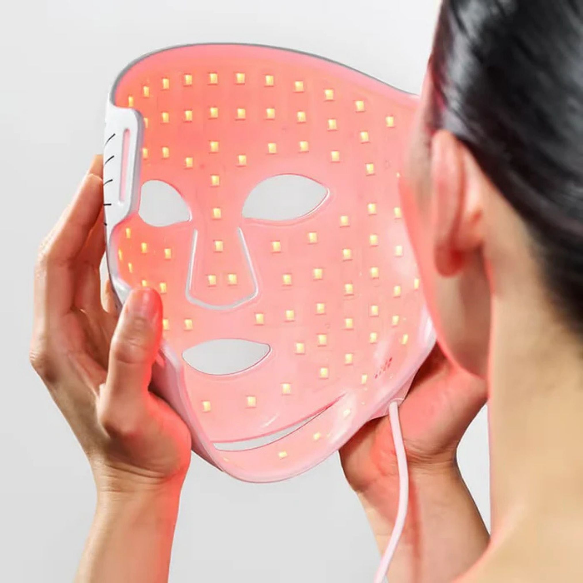 Personne tenant un masque facial lumineux. LED rouges allumées. Ouvertures pour les yeux, le nez et la bouche.