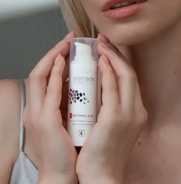 Flacon de sérum dans les mains. Inscription: Biotrade, Retinol 0,2%, Anti-Aging Serum. Bouchon transparent.
