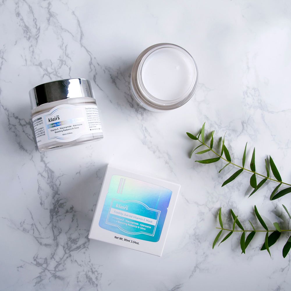 Drie producten op marmeren oppervlak. Pot en verpakking met opschrift: Dear, Klairs Freshly Juiced Vitamin E Mask. Plant.