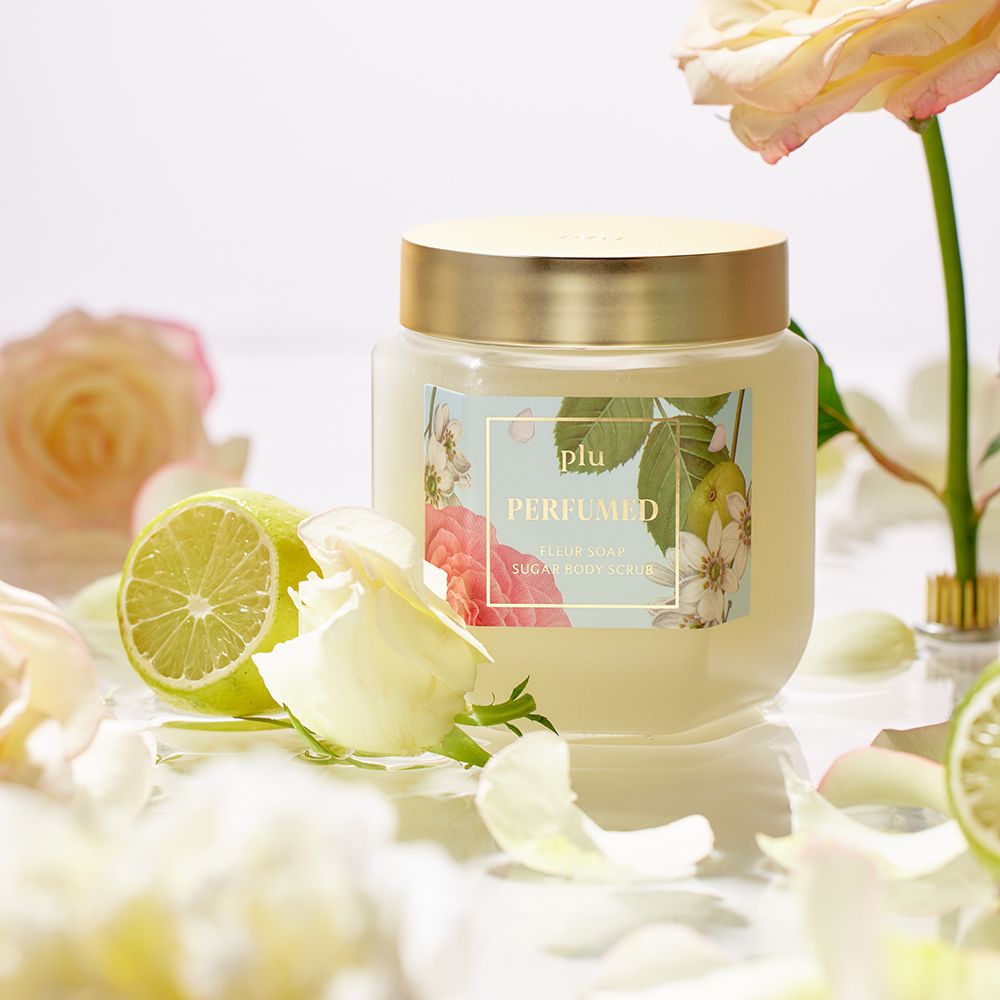 Pot en verre avec couvercle doré, entouré de fleurs et de tranches de citron vert. Étiquette avec motif floral et texte.