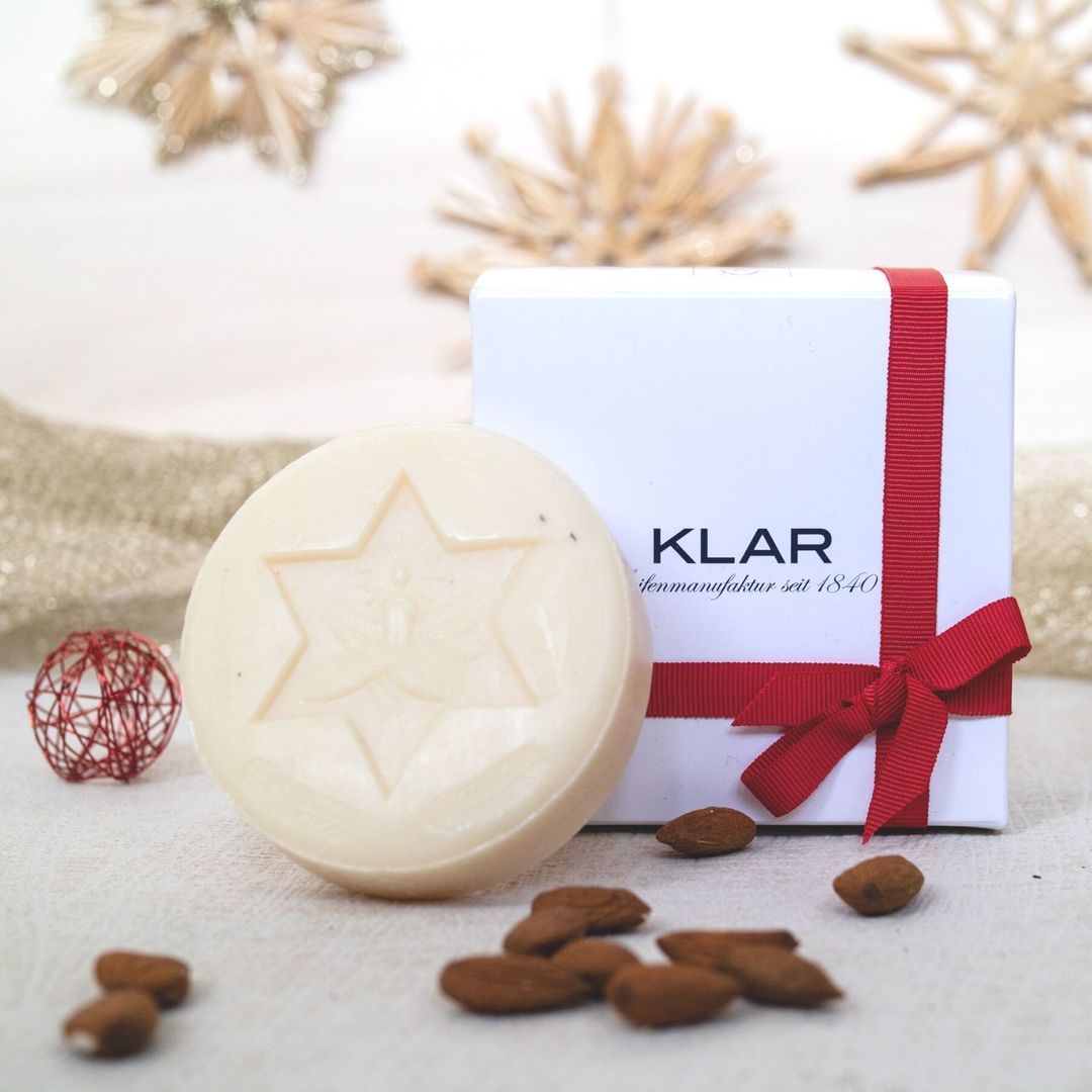 Savon rond avec motif étoile, amandes et coffret cadeau avec ruban rouge. Étoiles de paille et boule décorative rouge en arrière-plan.