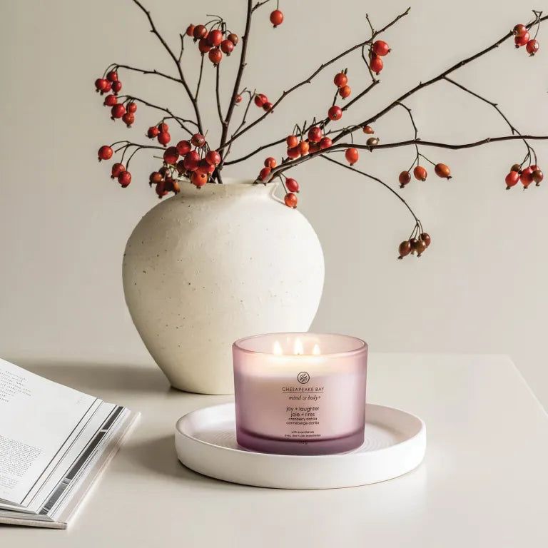 Bougie rose à trois mèches sur un plateau blanc. En arrière-plan, un vase avec des branches et des baies rouges. Inscription: Chesapeake Bay.