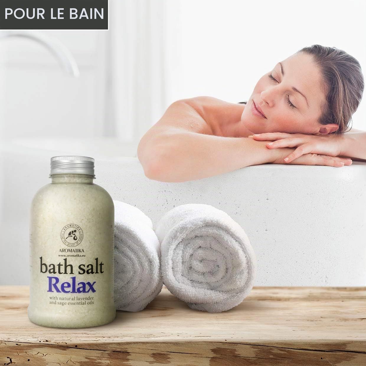 Bouteille de sel de bain 'Relax' avec lavande et huile de sauge. Deux serviettes roulées à côté.