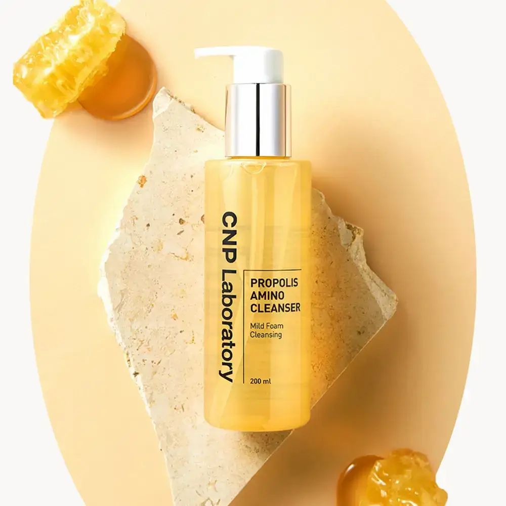 Gele fles met pomp. Opschrift: CNP Laboratory, Propolis Amino Cleanser, Mild Foam Cleansing. 200 ml. Op steen.