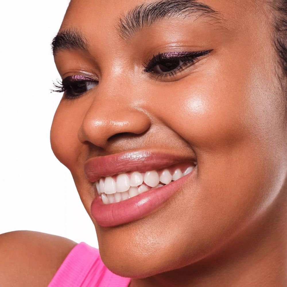 Gros plan d'une femme avec un eye-liner violet. Elle sourit.