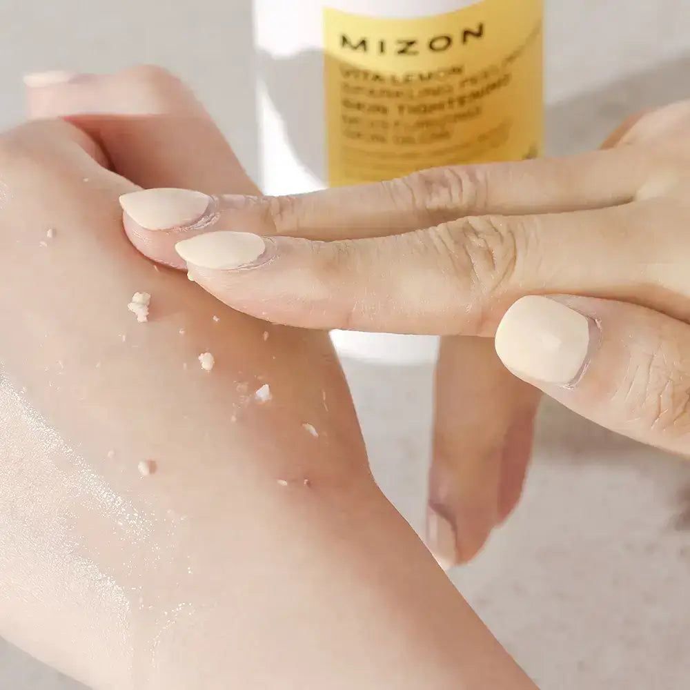 Handen wrijven gel op de huid. Gelresten zichtbaar. Product op de achtergrond. MIZON Vita Lemon Sparkling Peeling Gel.