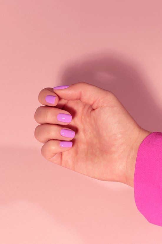 Main avec ongles vernis lilas. Fond rose. Manches d'un haut rose.