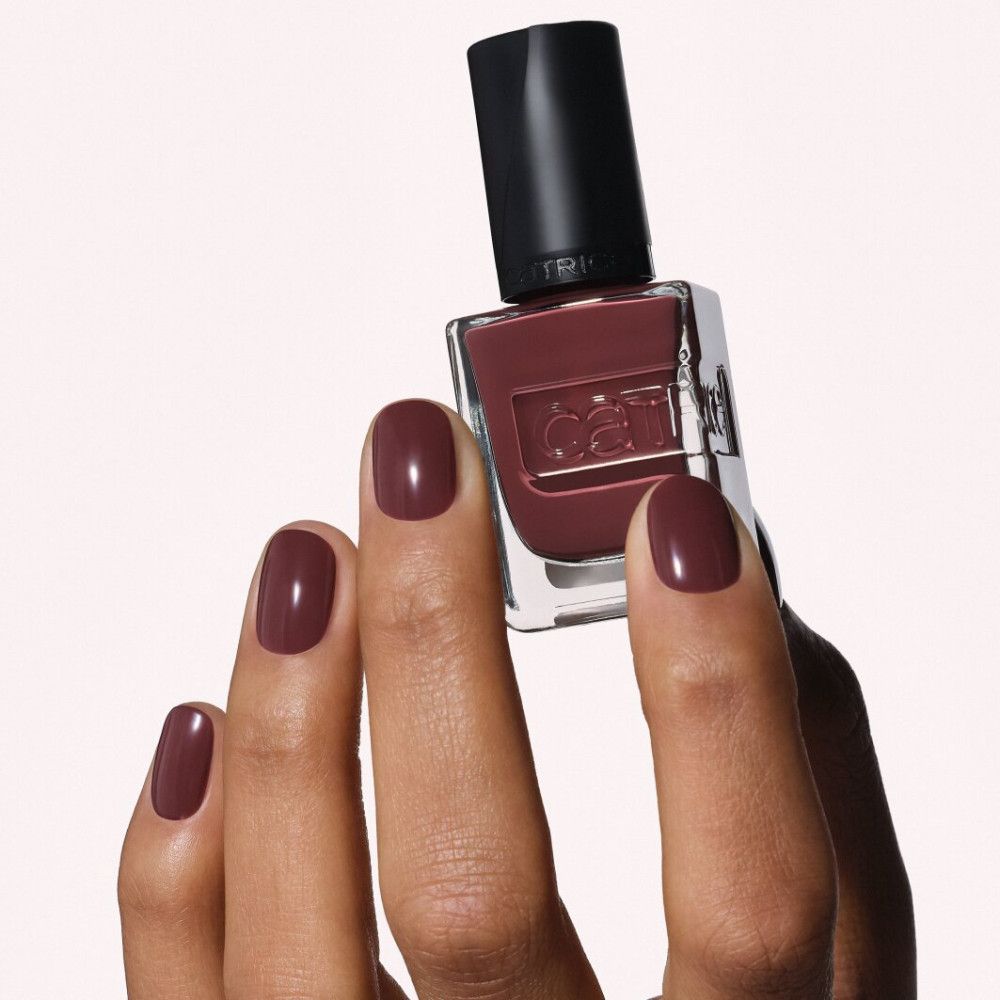 Een hand houdt een flesje donkerrode nagellak vast. De nagels zijn bijpassend gelakt.