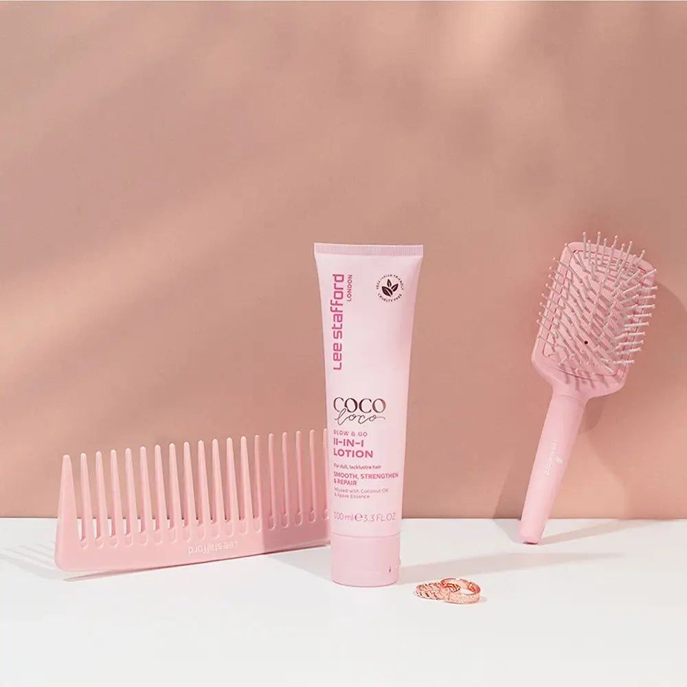 Lee Stafford Coco Loco Blow & Go 11-en-1 Lotion avec peigne et brosse à cheveux sur fond rose.