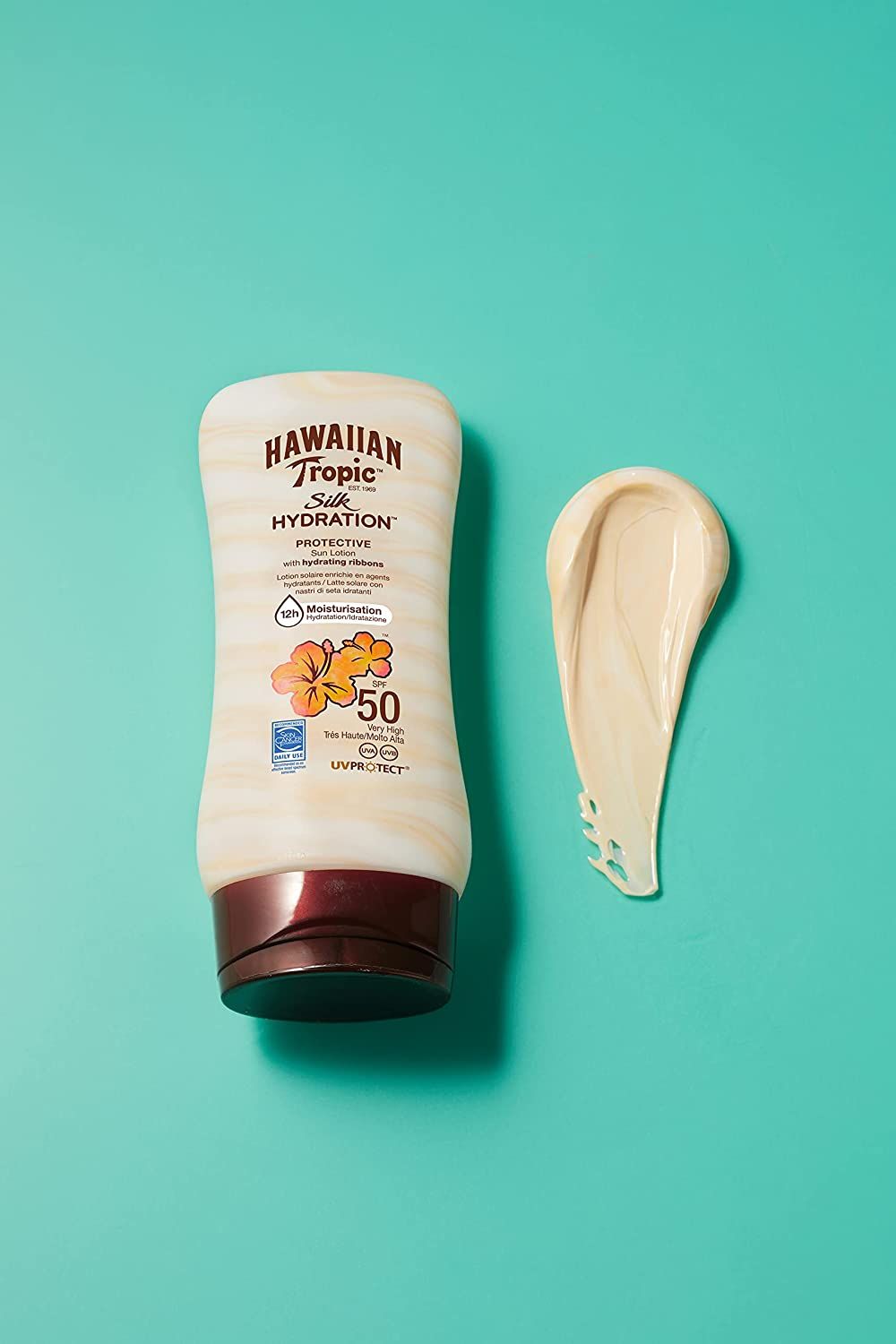 Flacon de lotion solaire Hawaiian Tropic Silk Hydration, SPF 50, à côté d'une goutte de lotion sur fond bleu.
