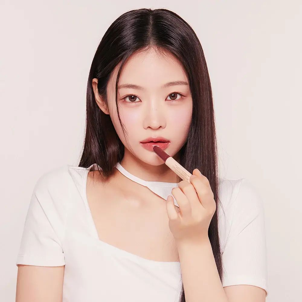 Jonge vrouw brengt lipgloss aan. Ze houdt een lipgloss-stift vast. De lipgloss is lichtbeige.