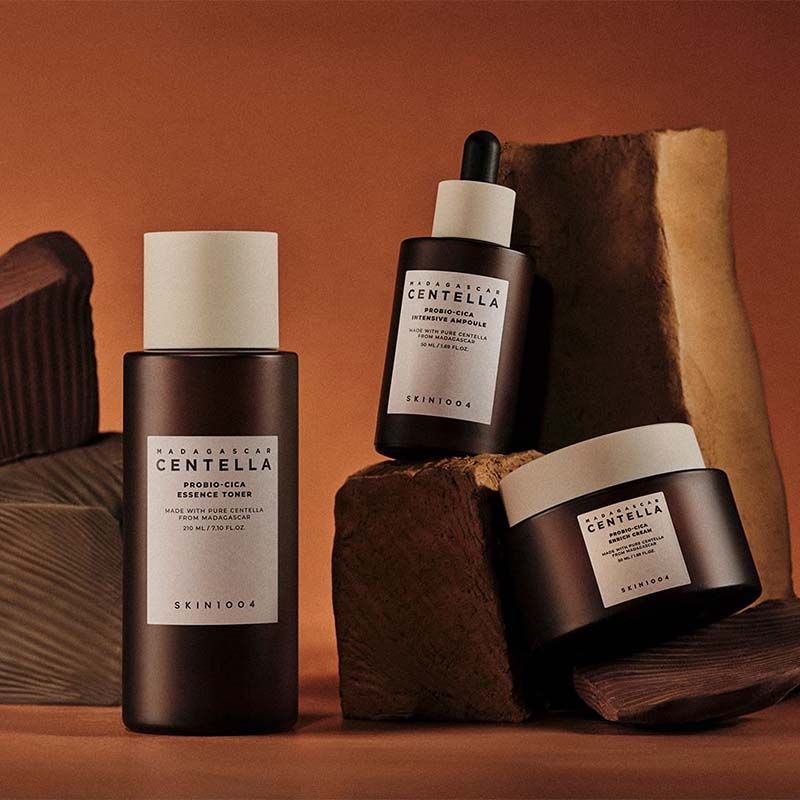 Trois bouteilles et pots bruns. Étiquette avec texte: MADAGASCAR CENTELLA, SKIN1004. Produits sur des pierres.