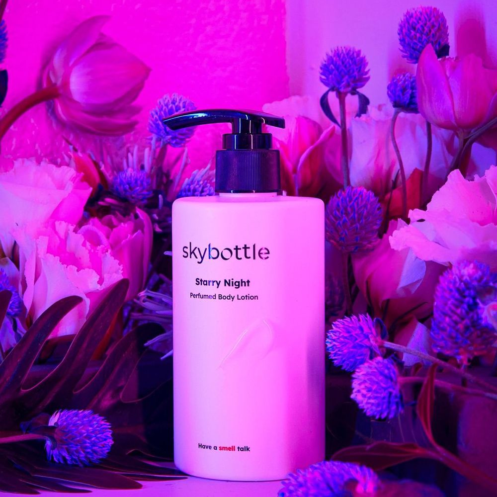 Witte fles met zwarte pomp, omringd door bloemen. Opschrift: skybottle, Starry Night, Perfumed Body Lotion.