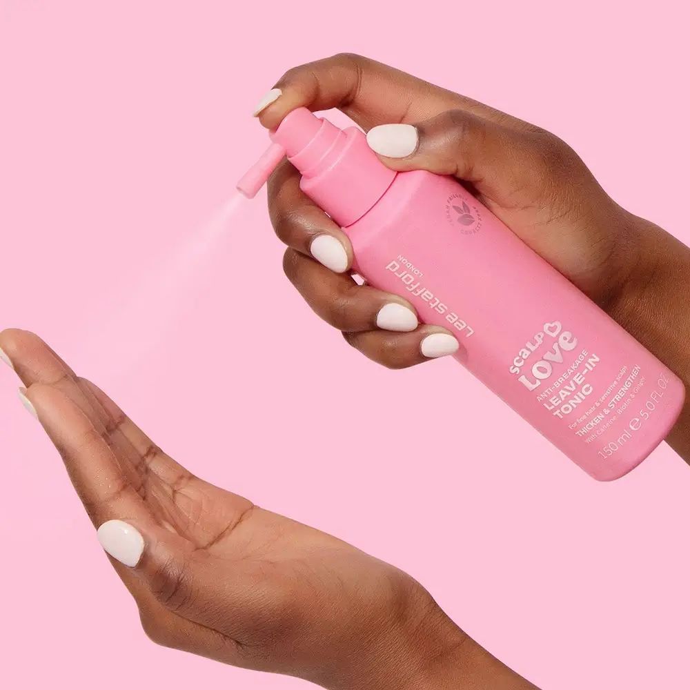Handen houden een roze spuitfles vast. Spuitnevel wordt gespoten. Opschrift: Lee Stafford, Scalp Love, Leave-In Tonic.