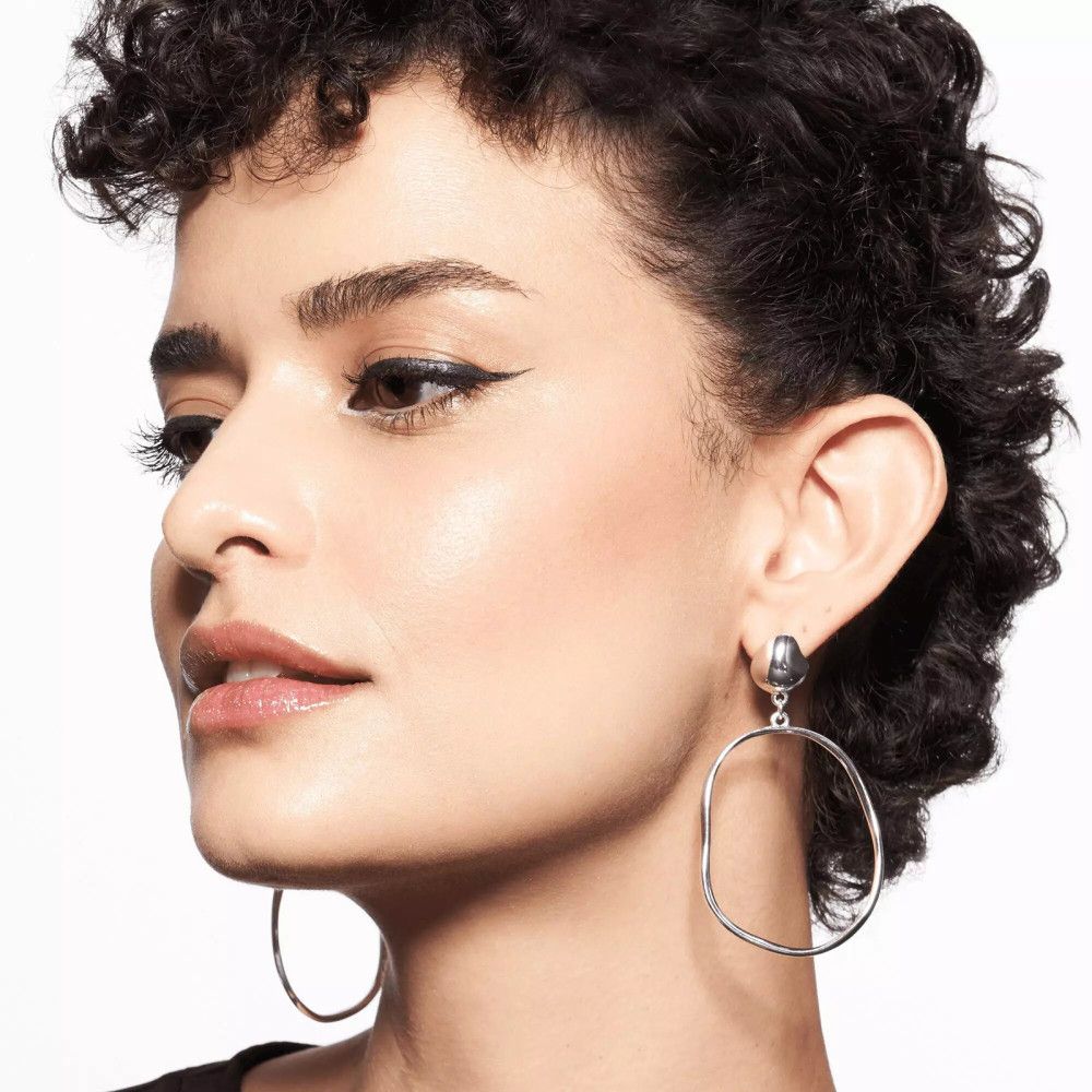 Portrait d'une femme avec eye-liner. Elle porte de grandes boucles d'oreilles rondes.