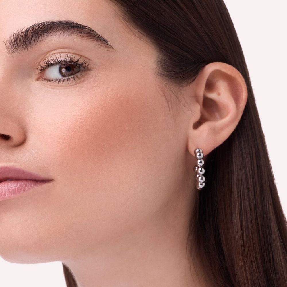 Gros plan d'une femme. Elle porte des boucles d'oreilles. Du blush est visible sur les joues.