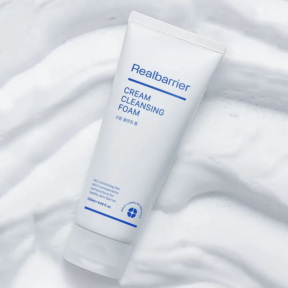 Witte tube met blauwe tekst. Opschrift: Realbarrier, CREAM CLEANSING FOAM. Op schuim gelegd.
