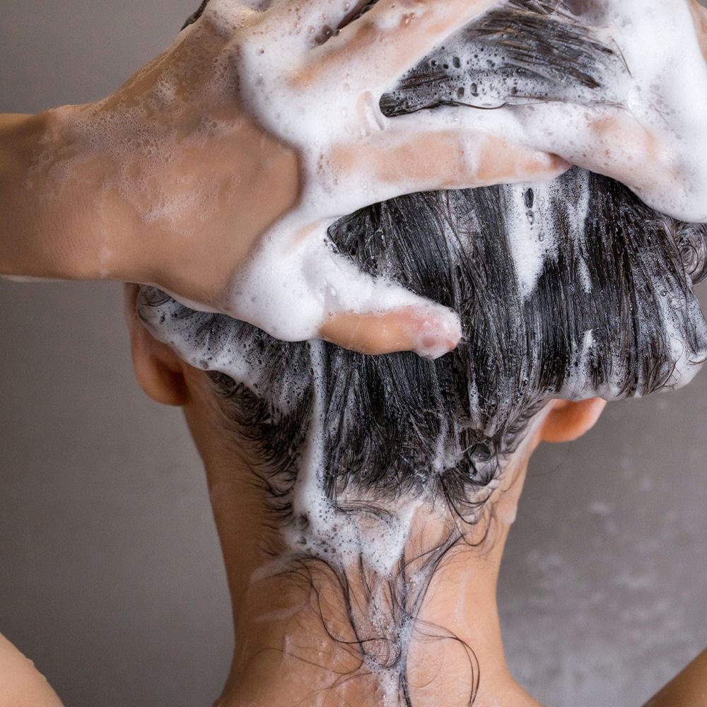Mains lavant les cheveux avec de la mousse. Vue arrière d'une personne. La mousse recouvre les cheveux et le cuir chevelu.