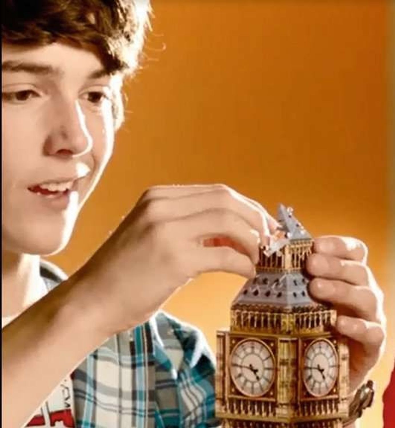 Jongen plaatst puzzelstukje op Big Ben. Goudkleurige en grijze elementen. Uurwerk zichtbaar. Oranje achtergrond.