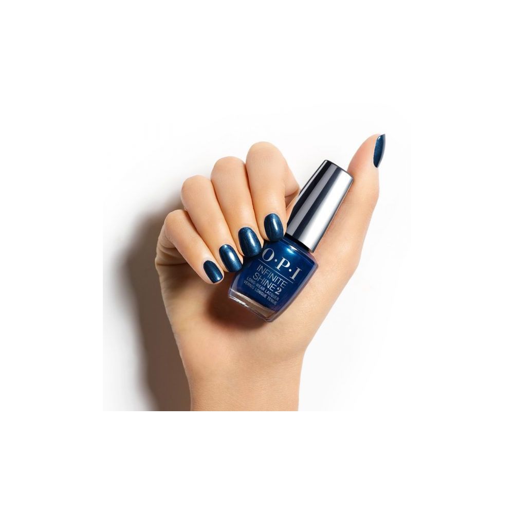 Main avec ongles vernis et flacon de vernis à ongles. Flacon à bouchon argenté, vernis bleu foncé. OPI Infinite Shine 2.
