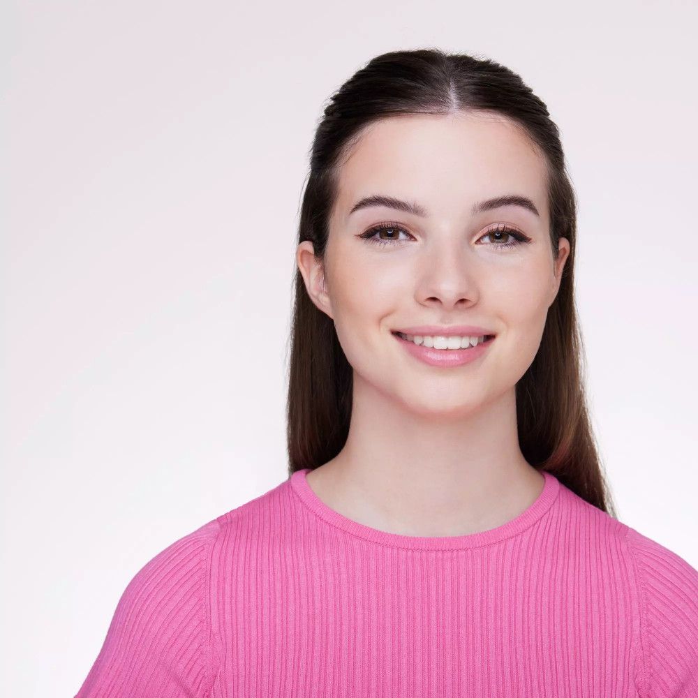 Portrait d'une femme avec un crayon pour les yeux. Elle sourit. Cheveux brun foncé. Haut rose.