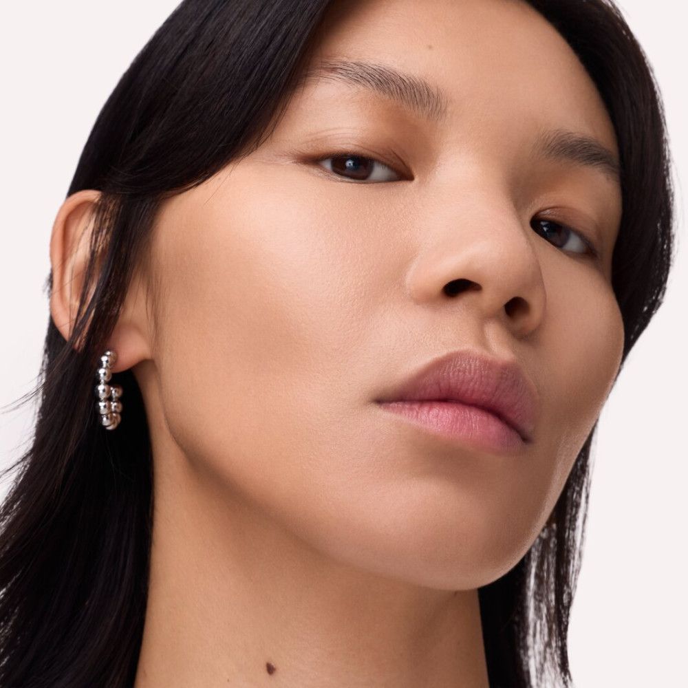 Gros plan d'une femme portant des boucles d'oreilles argentées. Les boucles d'oreilles sont rondes et texturées.