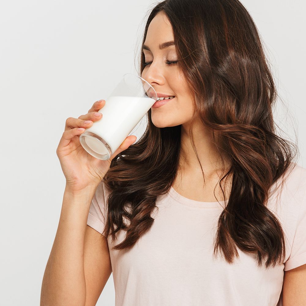 Gros plan d'une femme buvant du lait. Peau claire, cheveux bruns, haut rose.