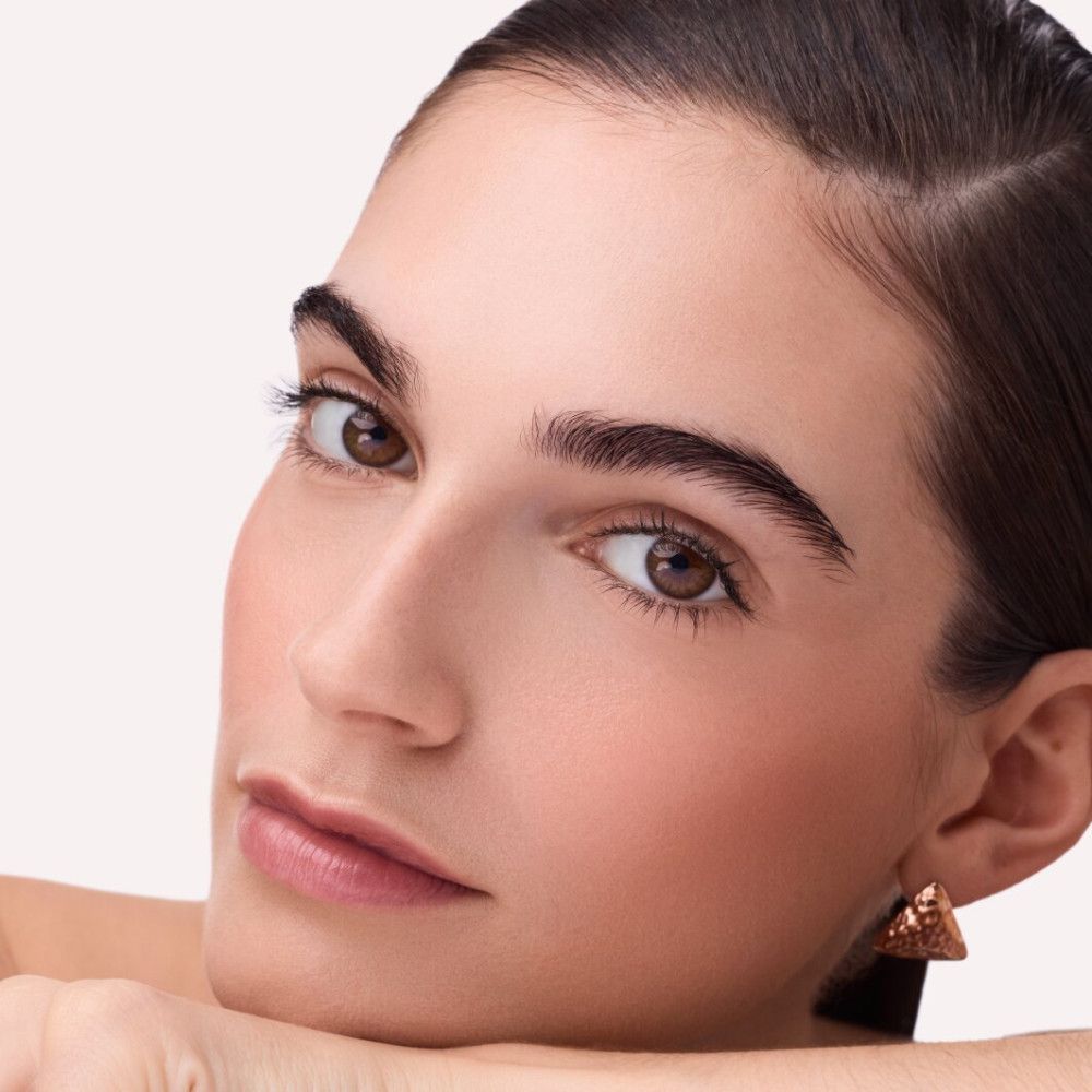 Gros plan d'une femme à la peau bronzée. Elle porte des boucles d'oreilles dorées. Du fard à joues est appliqué sur ses joues.