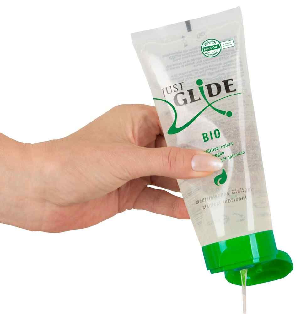 Main tenant un tube transparent avec bouchon vert. Inscription: JUST GLIDE BIO. Lubrifiant sortant du tube.