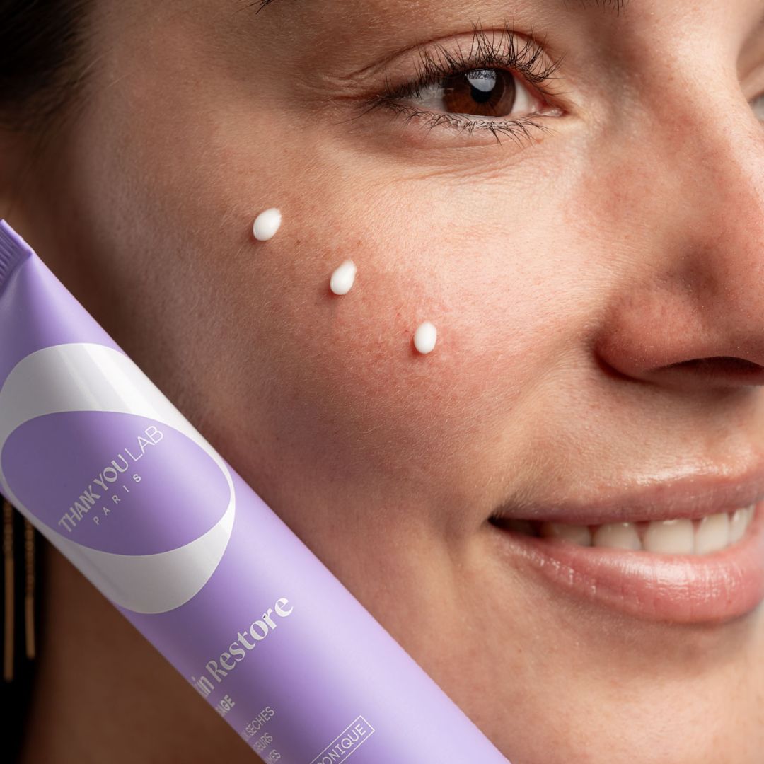 Paarse tube met witte crème. Drie crème-stippen op de huid. Opschrift: THANK YOU LAB PARIS.