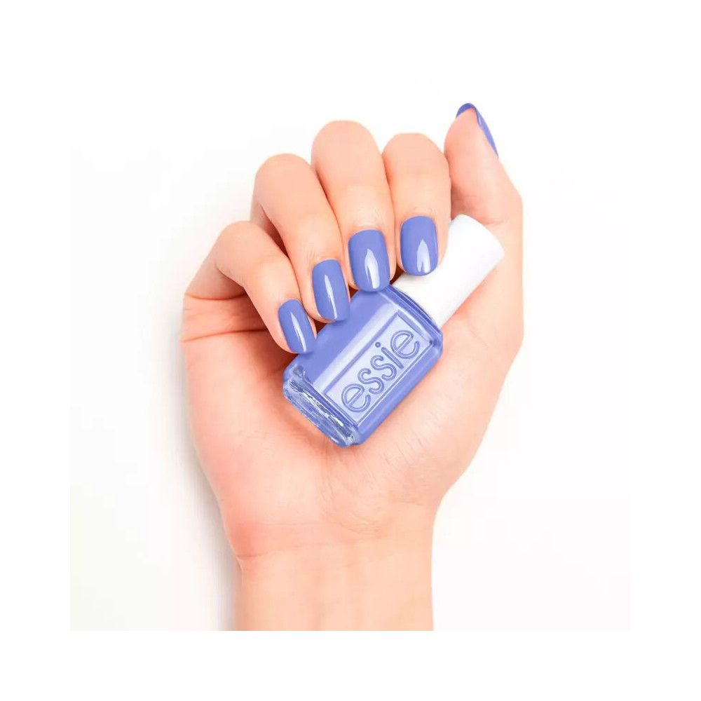 Hand met gelakte nagels en nagellakfles. Fles met witte dop, lichtpaarse kleur, Essie-logo.