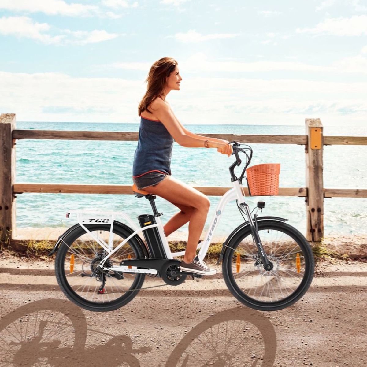 Vrouw op witte elektrische fiets met mand. Bruin zadel en handvatten. TTGO-logo. Achtergrond: zee.