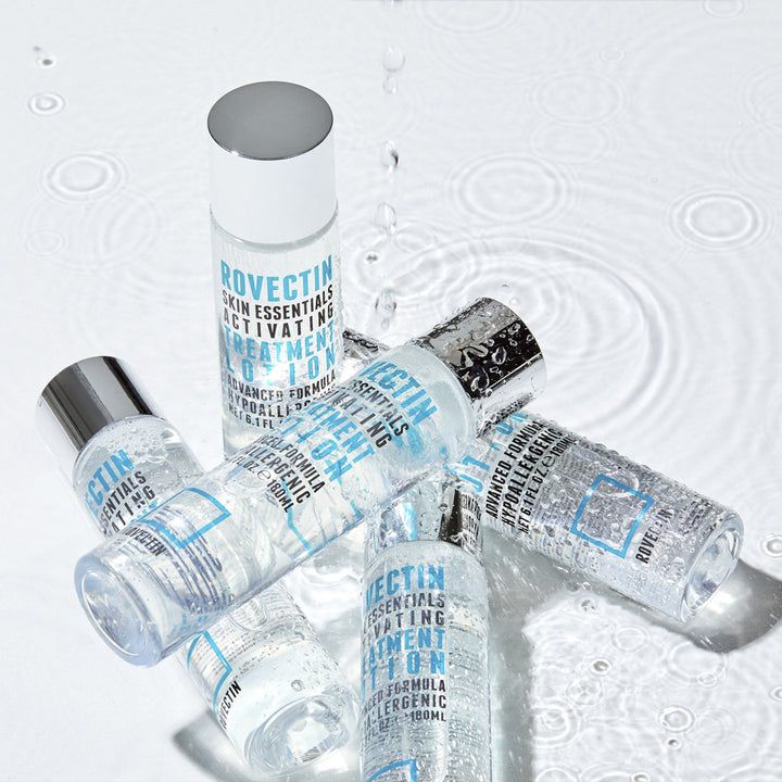Meerdere flessen met zilveren doppen, omringd door water. Opschrift: ROVECTIN Skin Essentials Activating Treatment Lotion.