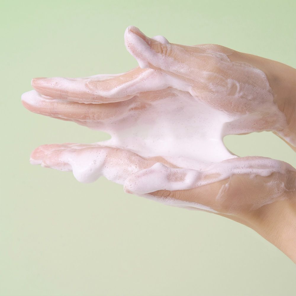 Mains avec un produit nettoyant moussant débordant entre les doigts.