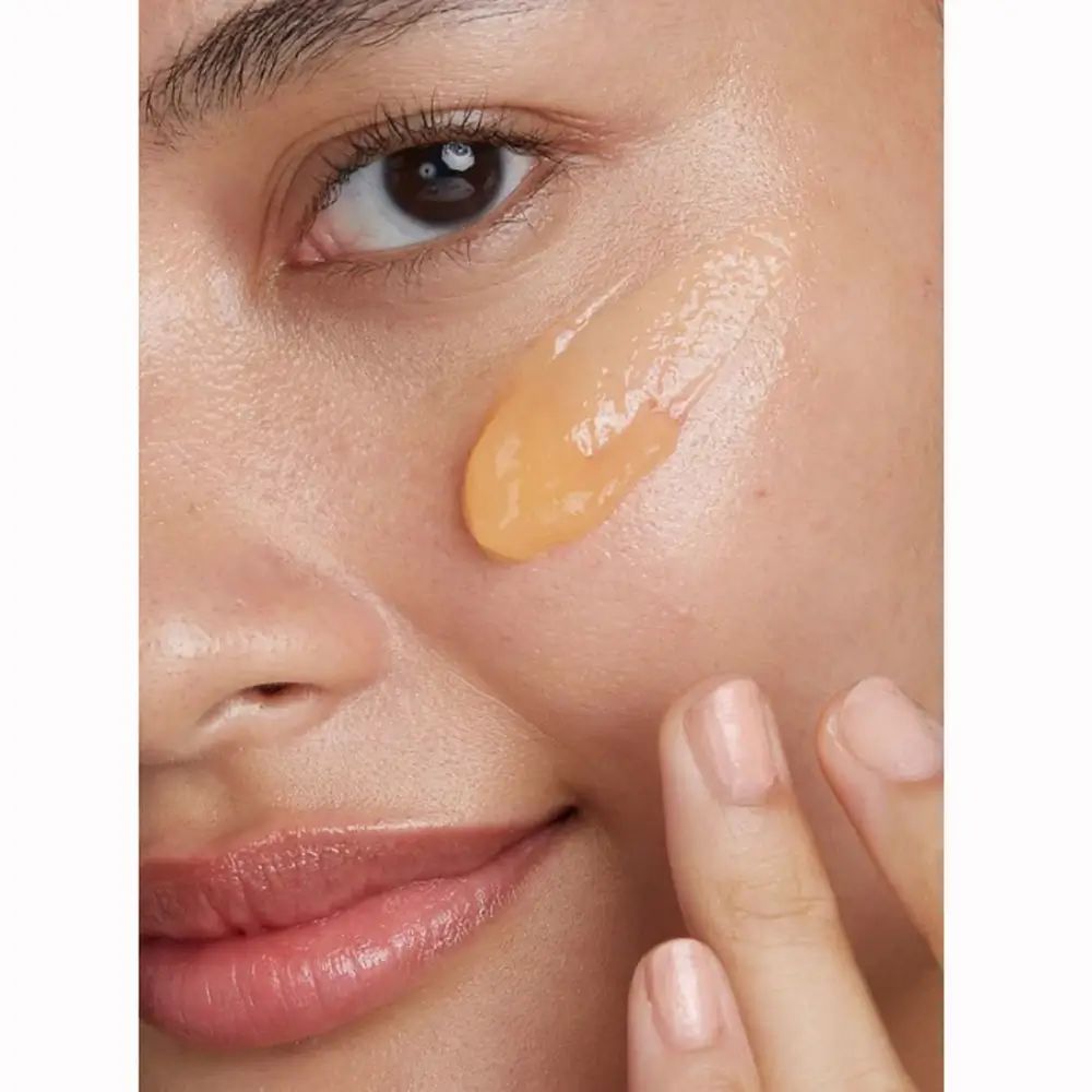 Close-up van een gezicht met aangebrachte, gelige reinigingslotion. Huidgedeelte aangeraakt met een vinger.