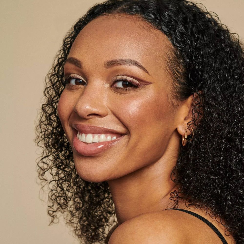 Portrait d'une femme souriante avec des boucles. Les sourcils sont mis en valeur.