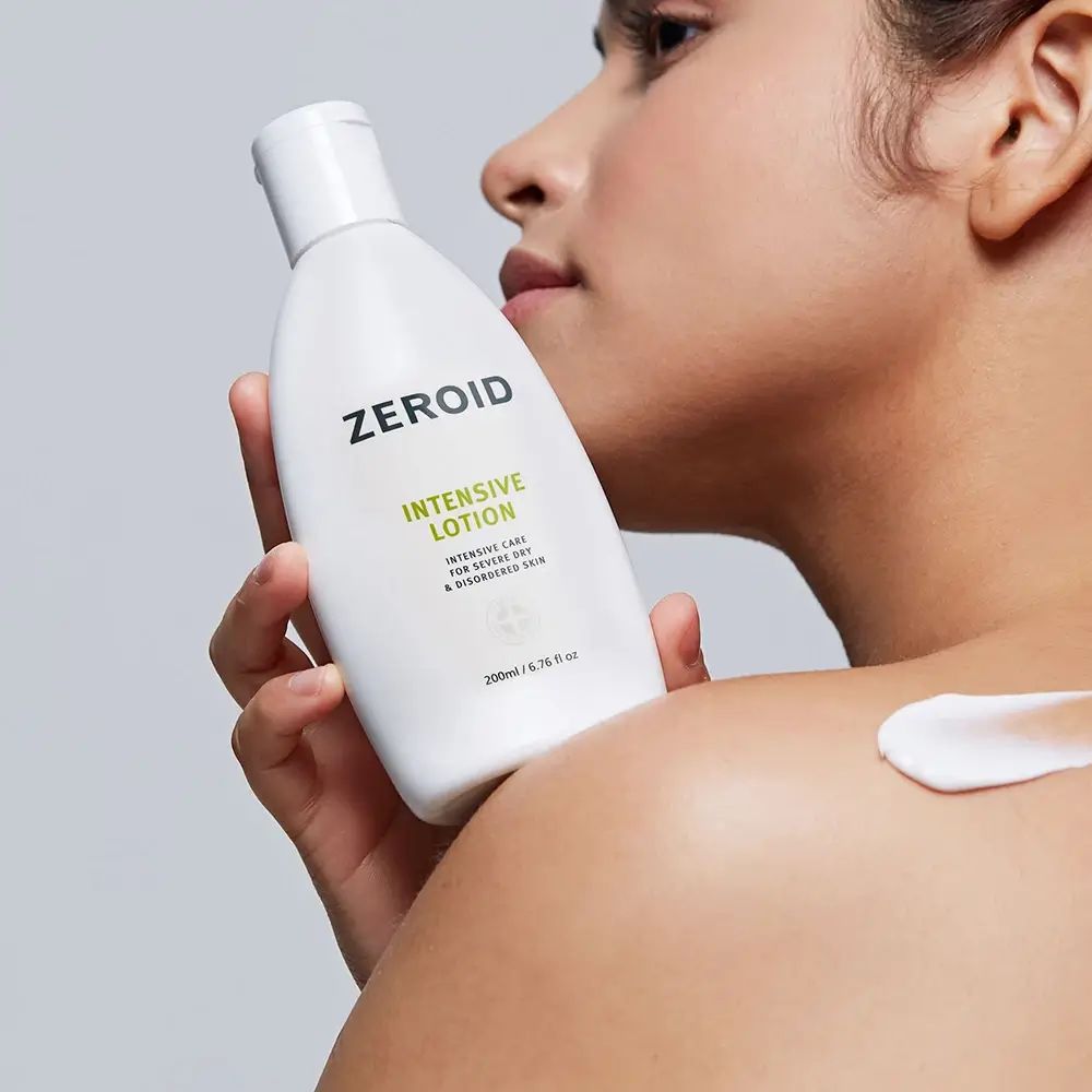 Personne tenant un flacon de ZEROID Intensive Lotion. Crème appliquée sur l'épaule. Texte vert.