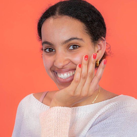 Lachende vrouw met rode nagellak. Ze houdt haar hand voor haar gezicht.