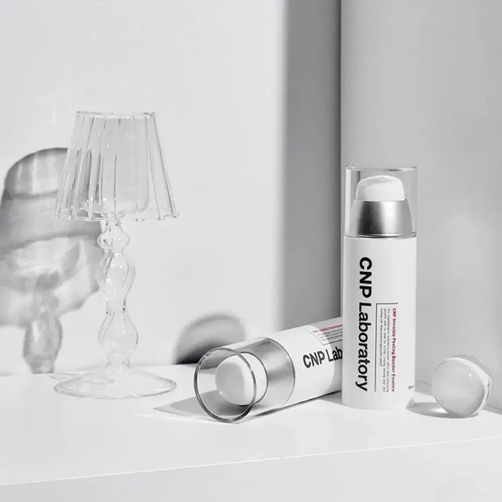 Twee witte flessen met zilveren pompen. Opschrift: CNP Laboratory. Eén fles ligt.