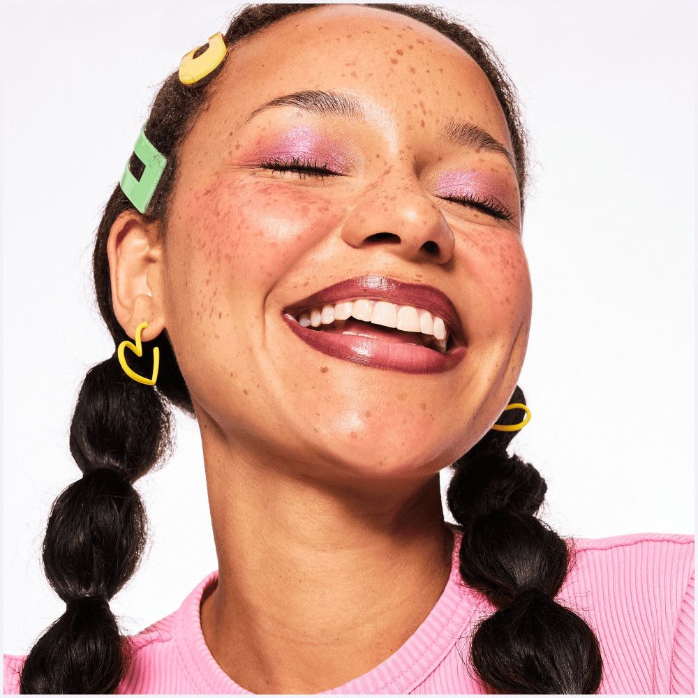 Lachende vrouw met lippenstift. Gele oorbellen. Vlechten. Kleur van de lippenstift zichtbaar.