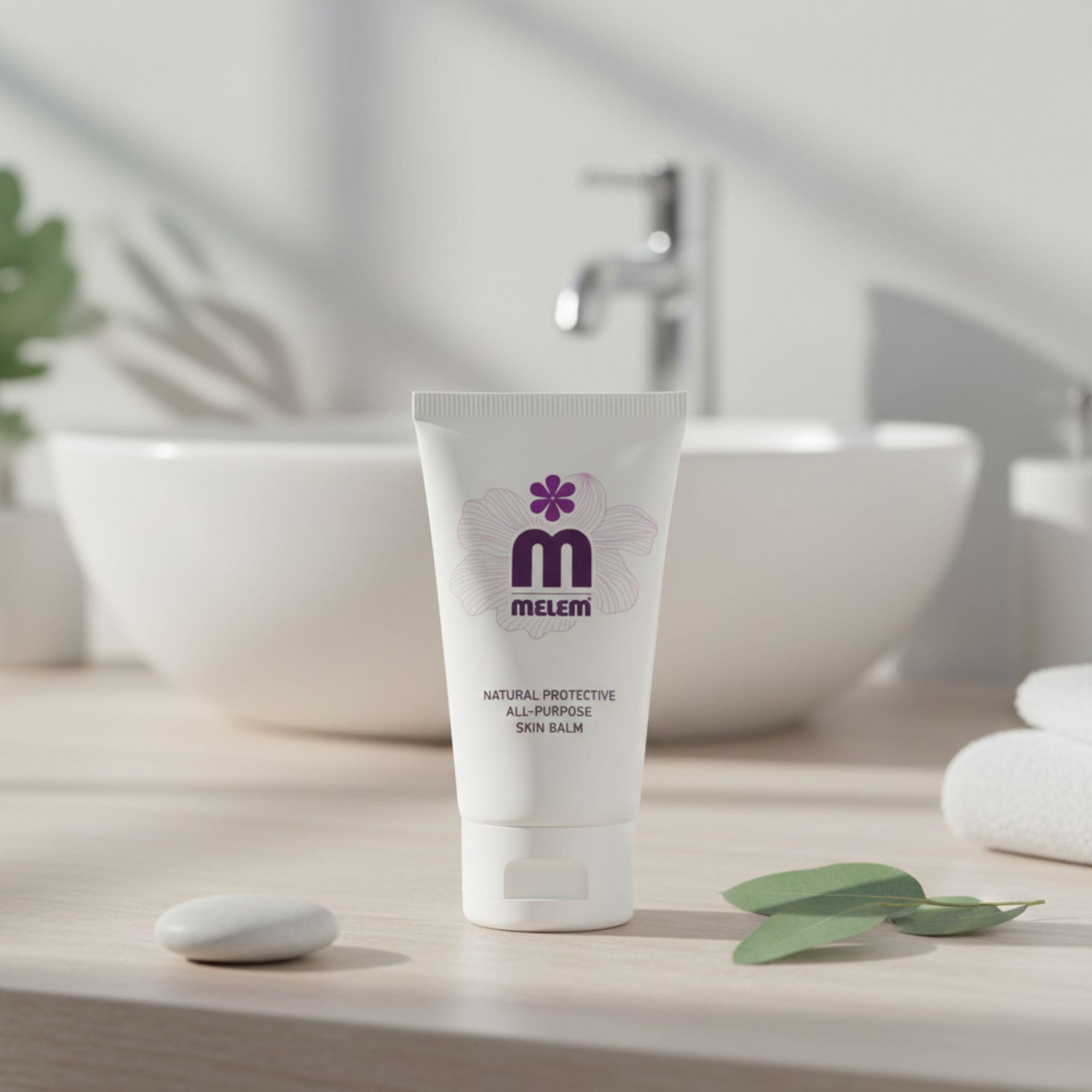 Tube blanc avec logo violet et texte: Melem, Natural Protective All-Purpose Skin Balm. Placé devant un lavabo.