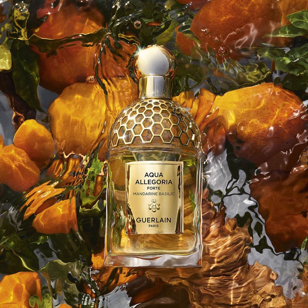 Guerlain Aqua Allegoria Forte fles in water. Gouden details, bijenlogo. Omringd door sinaasappels en bladeren.
