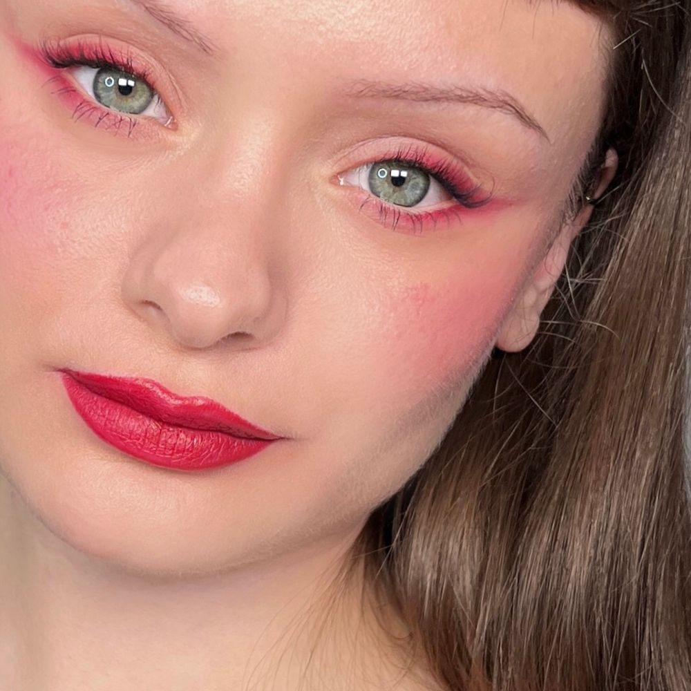 Gros plan d'un visage avec rouge à lèvres, fard à joues et eye-liner rouges. Yeux verts.