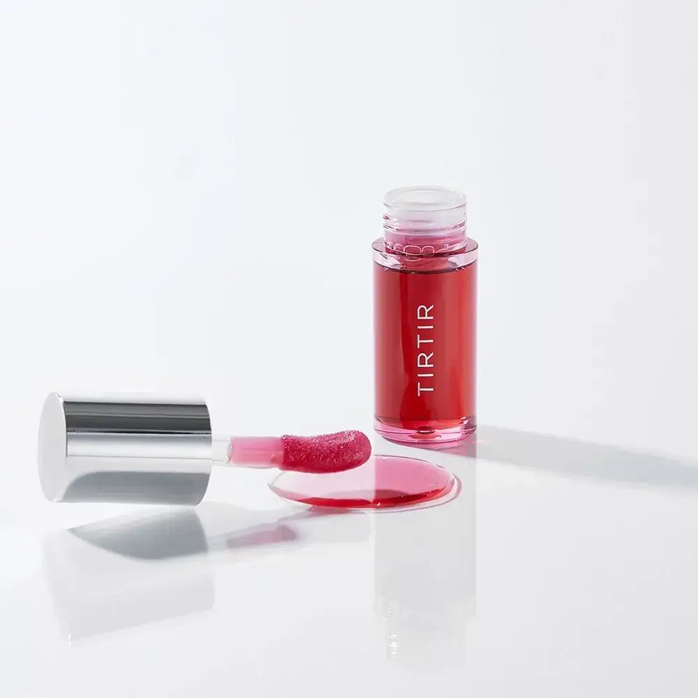 Un flacon de TIR TIR My Glow Lip Oil Rosy avec une goutte renversée et un applicateur ouvert.